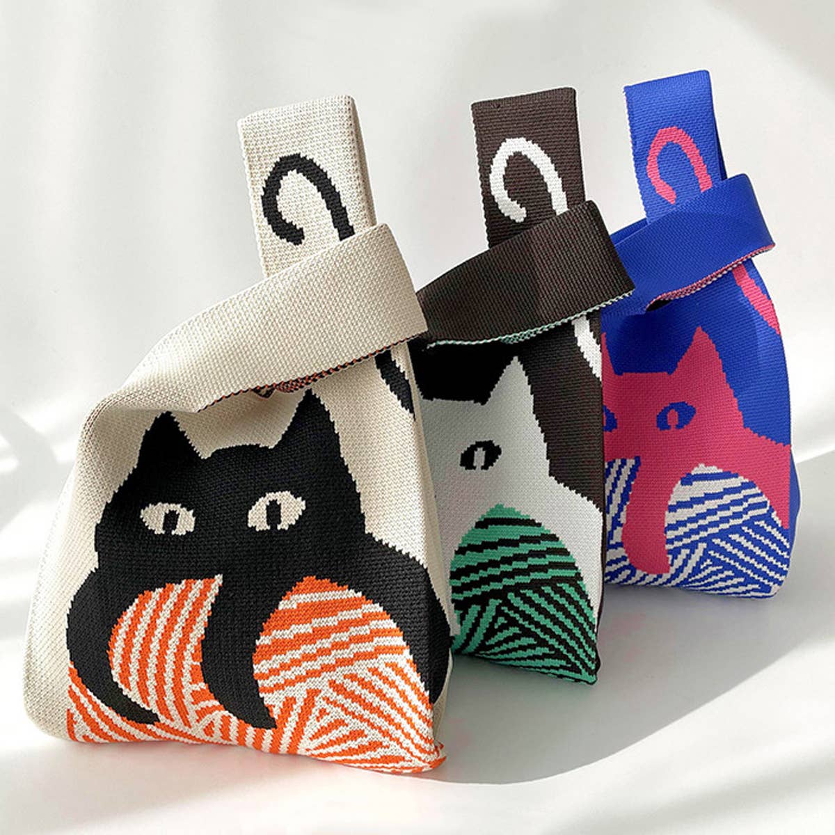 Three knit cat bags in cream, brown and blue, each with a different cat graphic