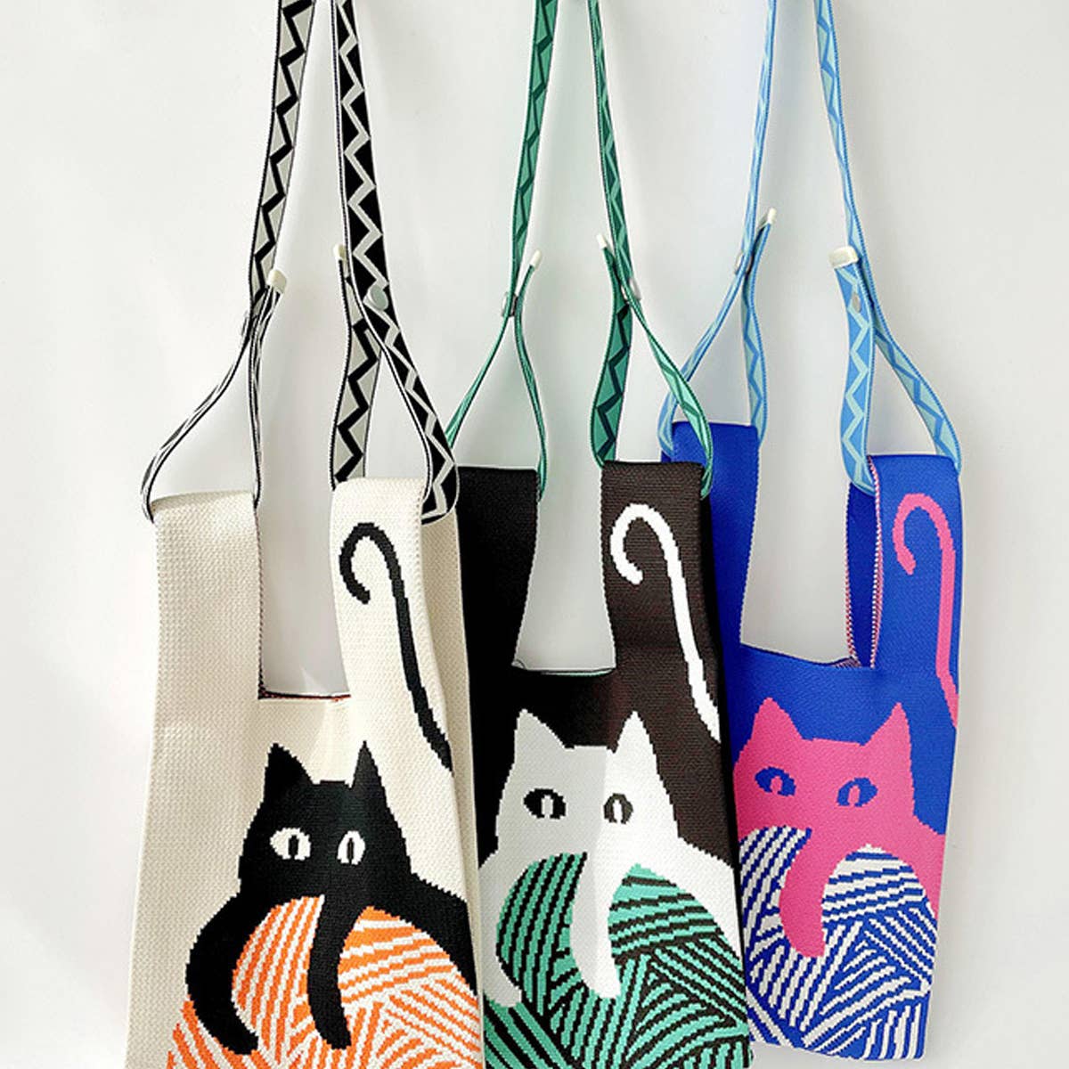 Three knit cat bags hanging from woven and braided straps