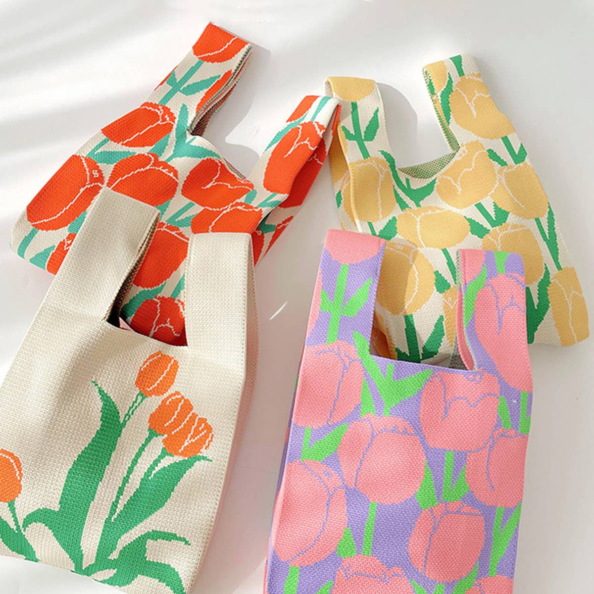 Several floral knit bags in cream, pink and yellow prints piled together