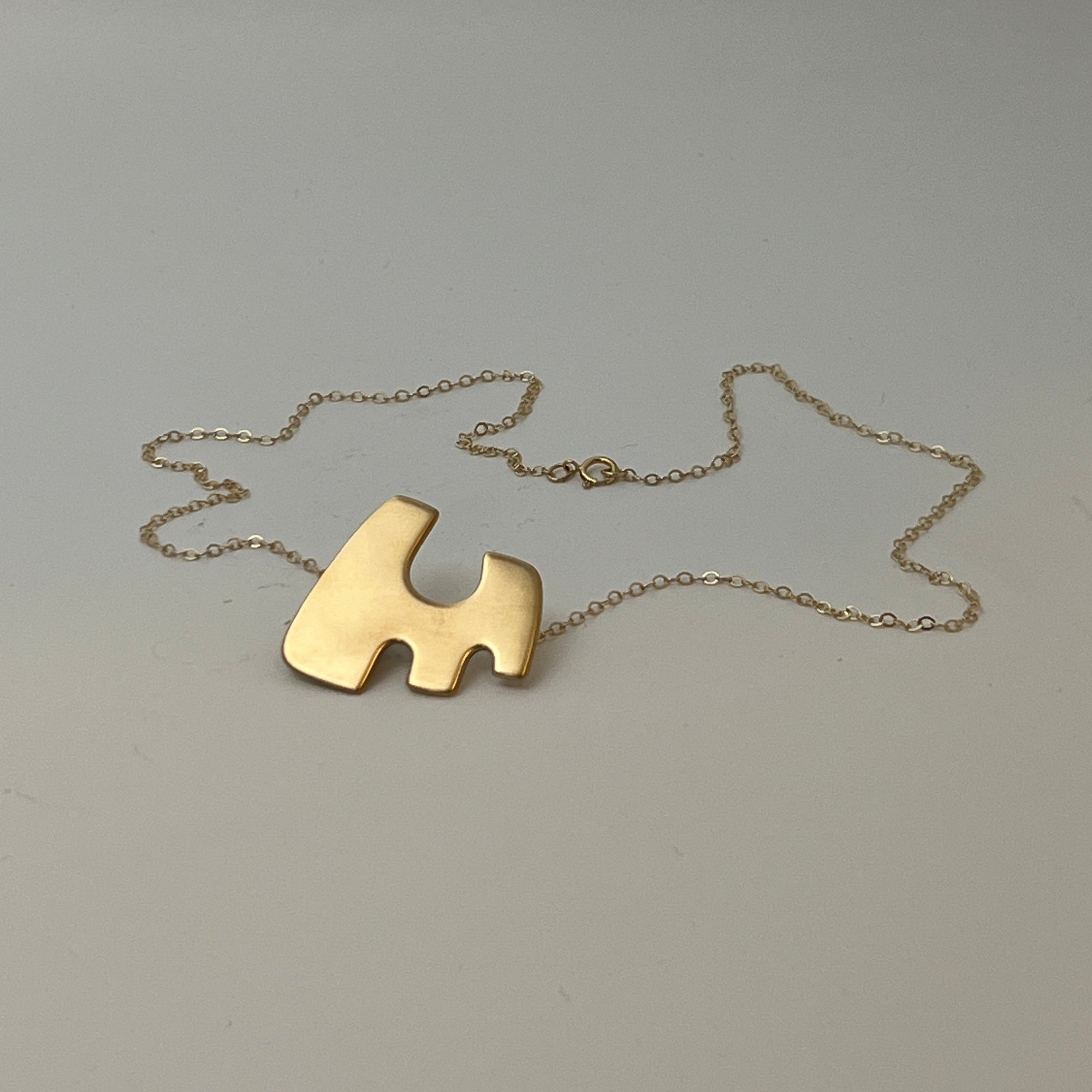 A silver, copper, and brass pendant necklace with a geometric cut-out design, displayed against a plain background.