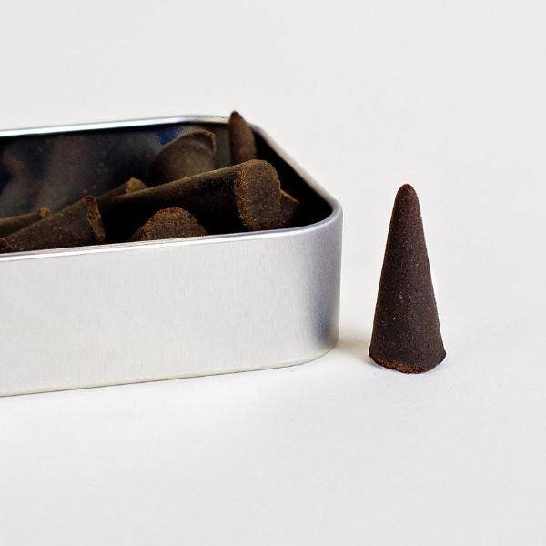 Incense cones in a metal box with one cone on a white surface