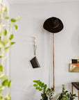 Black leather clutch hanging on a wall hook beside a hat and plants