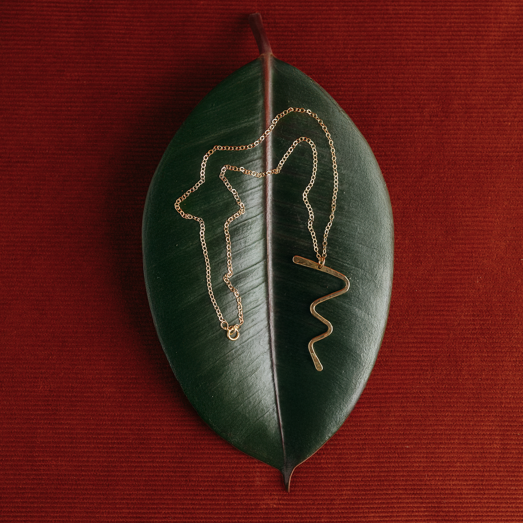 A pair of delicate gold chain necklaces draped over a dark green leaf, set against a textured dark red background.