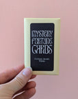 Hand holding a box of 'Mystery Fortune Cards' against a pink background
