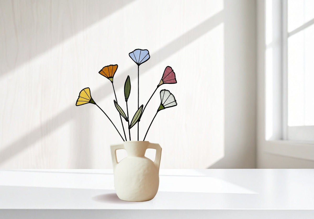 Stained glass wildflowers in yellow, orange, blue, pink and white in a white handled vase by a window