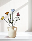 Stained glass wildflowers in yellow, orange, blue, pink and white in a white handled vase by a window