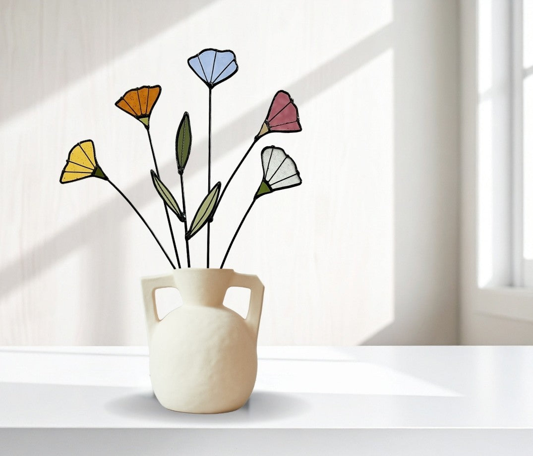 Five stained glass wildflower stems in a white handled vase in a bright white room