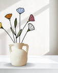 Five stained glass wildflower stems in a white handled vase in a bright white room