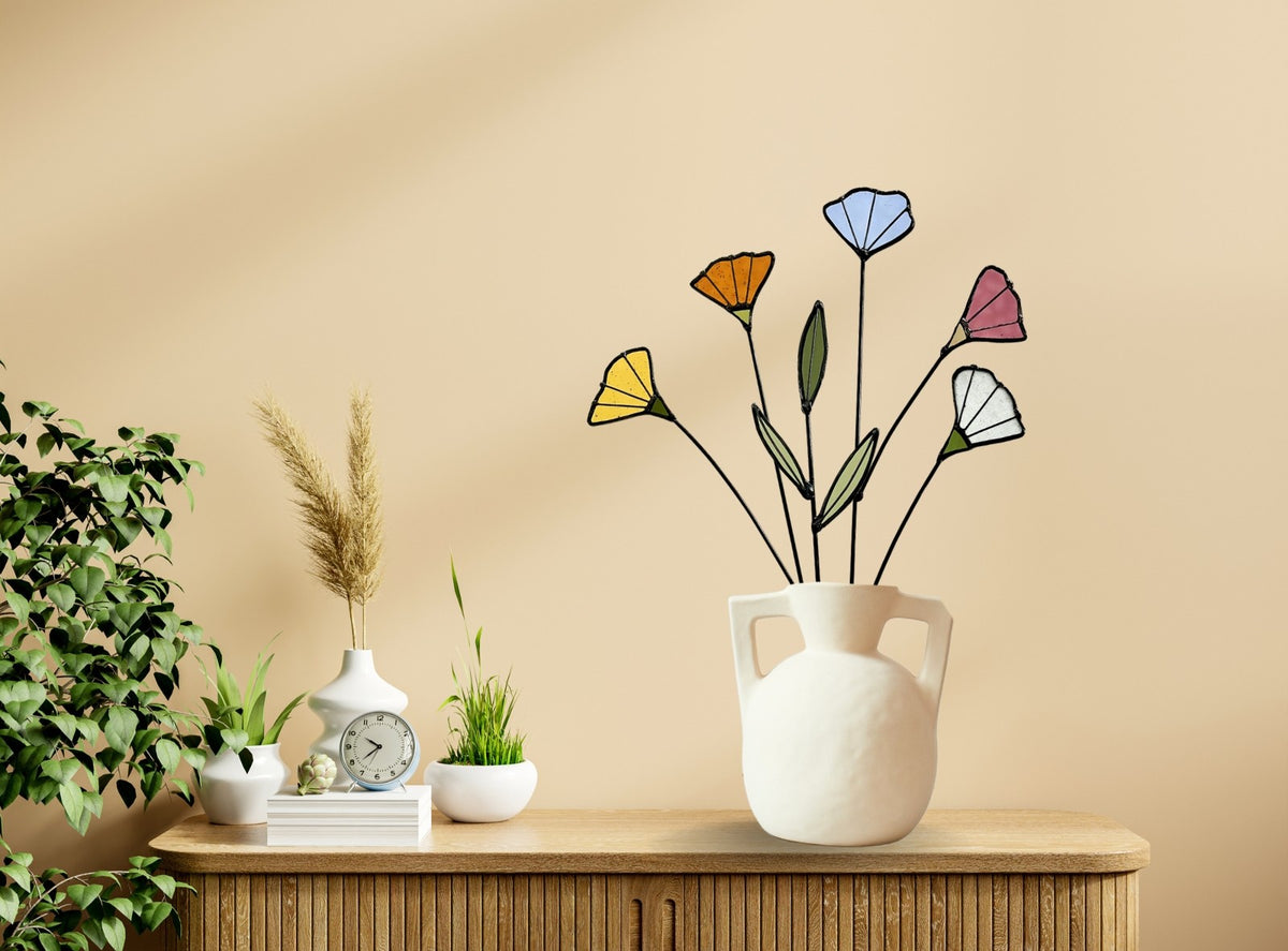 Stained glass wildflowers in a white handled vase on a wooden console beside plants
