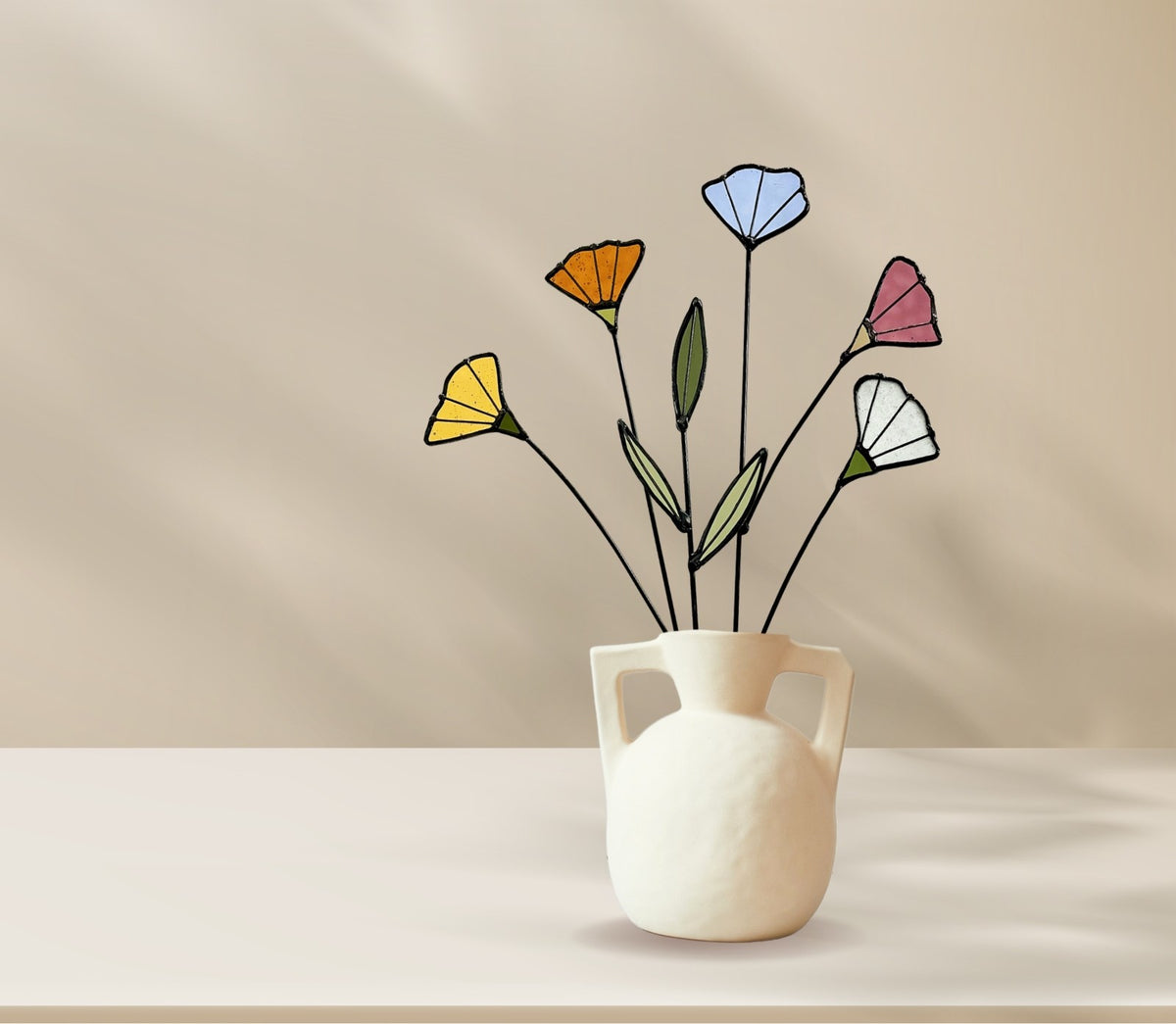 Stained glass wildflowers in a white handled vase on a beige table