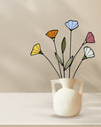 Stained glass wildflowers in a white handled vase on a beige table