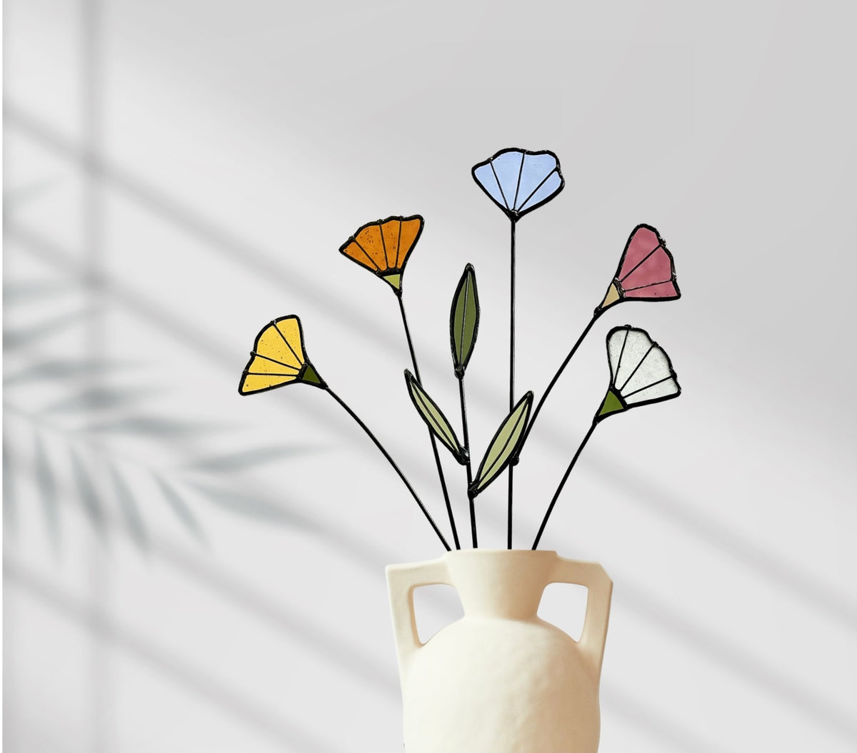 Stained glass wildflowers in a white handled vase against a gray wall with shadows