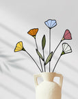 Stained glass wildflowers in a white handled vase against a gray wall with shadows
