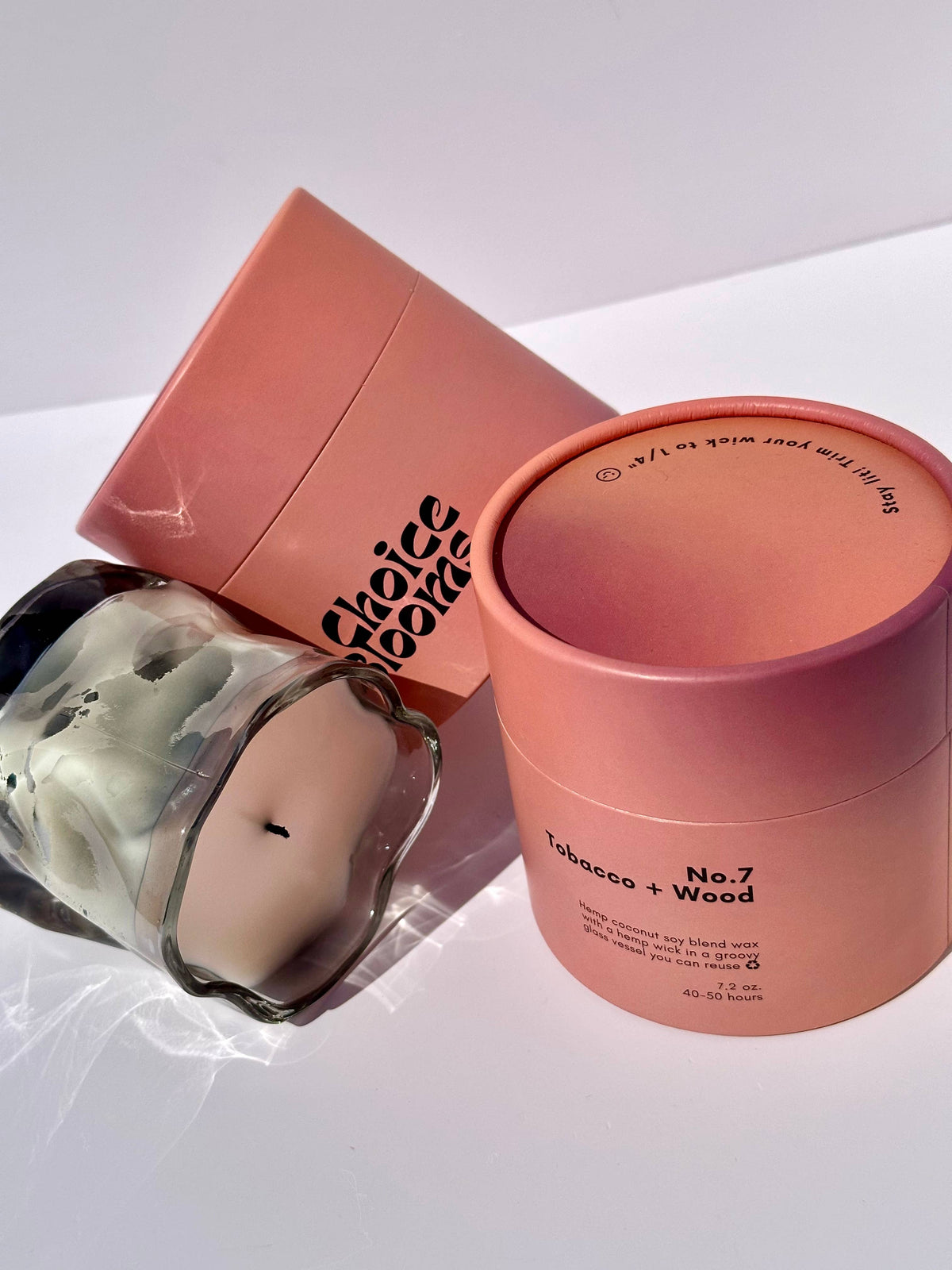 Smoky gray wavy glass candle beside an open pink box on white