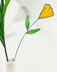 Single stained glass yellow tulip stem in a white vase beside a green palm leaf