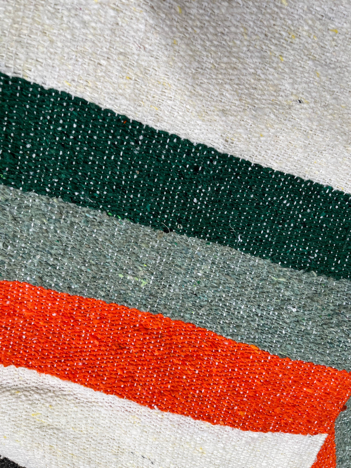 Close-up of green, sage and orange stripes woven into a cream blanket