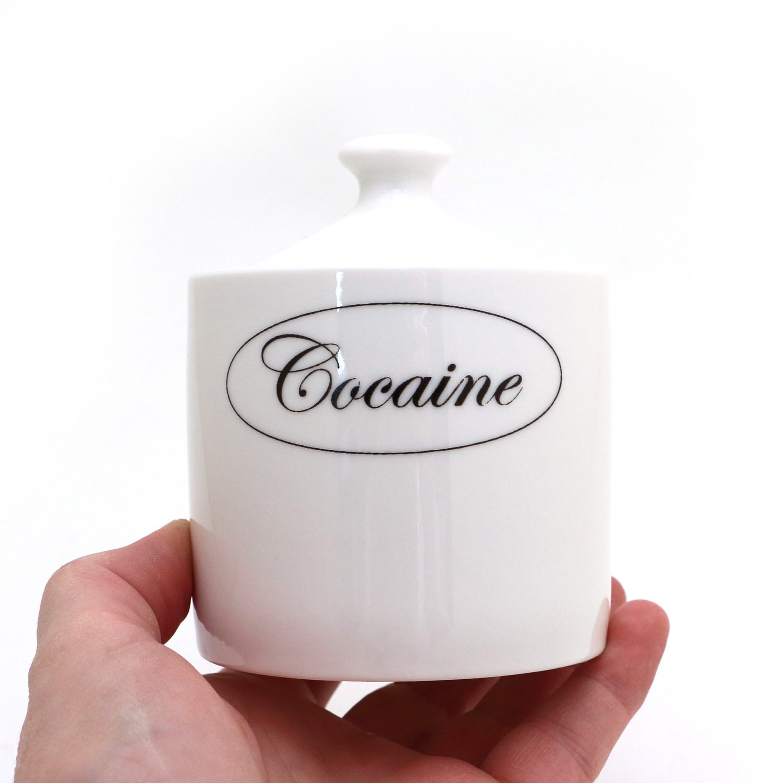 White container with 'Cocaine' label held by a hand on a white background