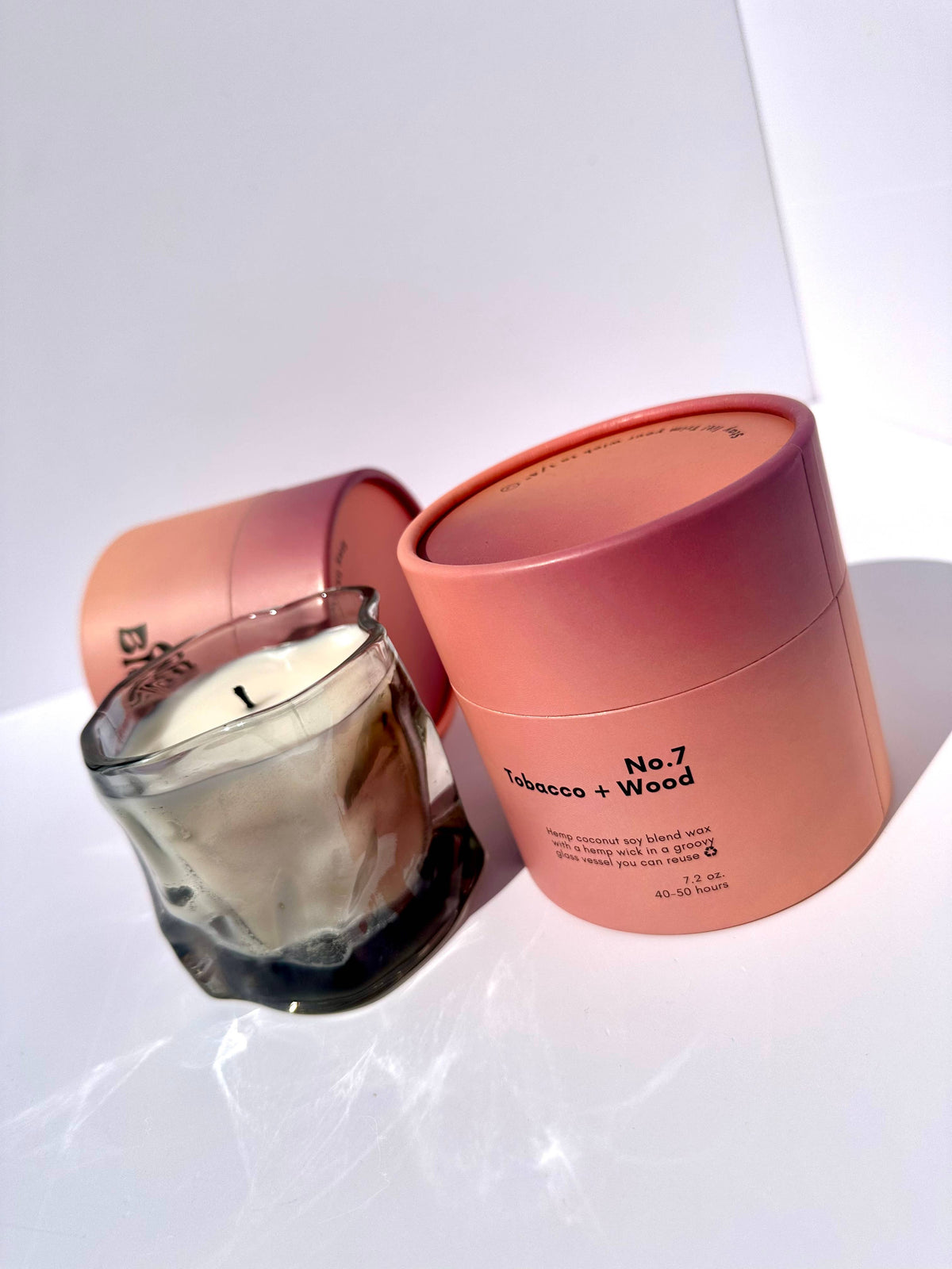 Smoky gray wavy glass candle in front of an open pink box in bright light