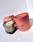 Smoky gray wavy glass candle in front of an open pink box in bright light