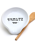 White bowl with 'SHMUTZ' text and a wooden spoon on a white background