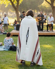 Person wrapped in a cream Desert Mesa blanket watching a band play in a park
