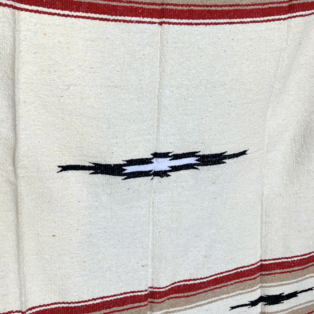 Close-up of a black and white diamond motif and red stripe on a cream woven blanket