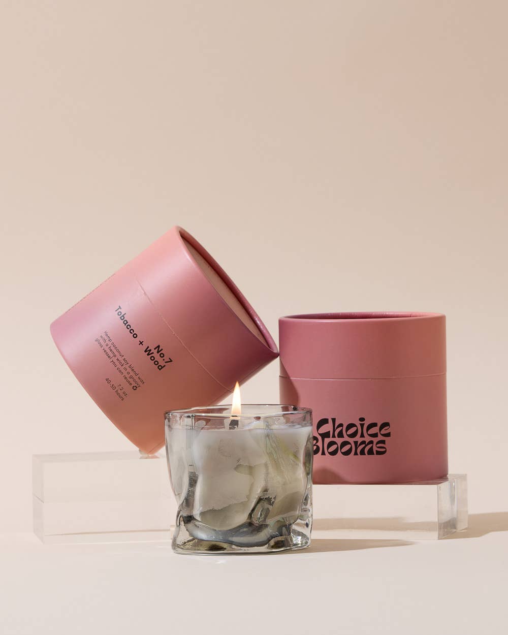 Smoky gray wavy glass candle in front of stacked pink boxes on a clear riser