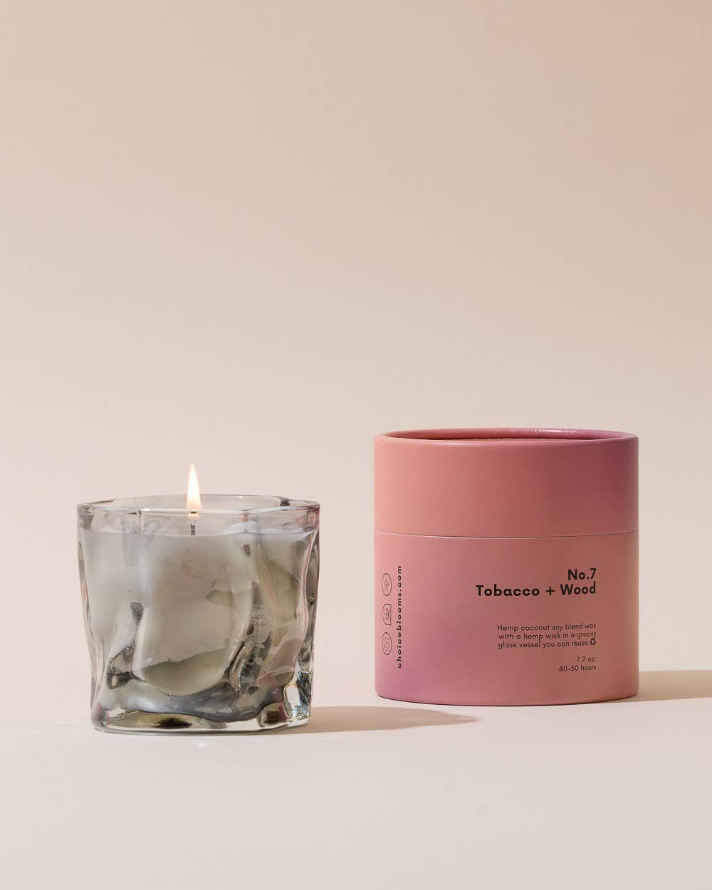 Smoky gray wavy glass candle beside a pink cylindrical box on a cream backdrop
