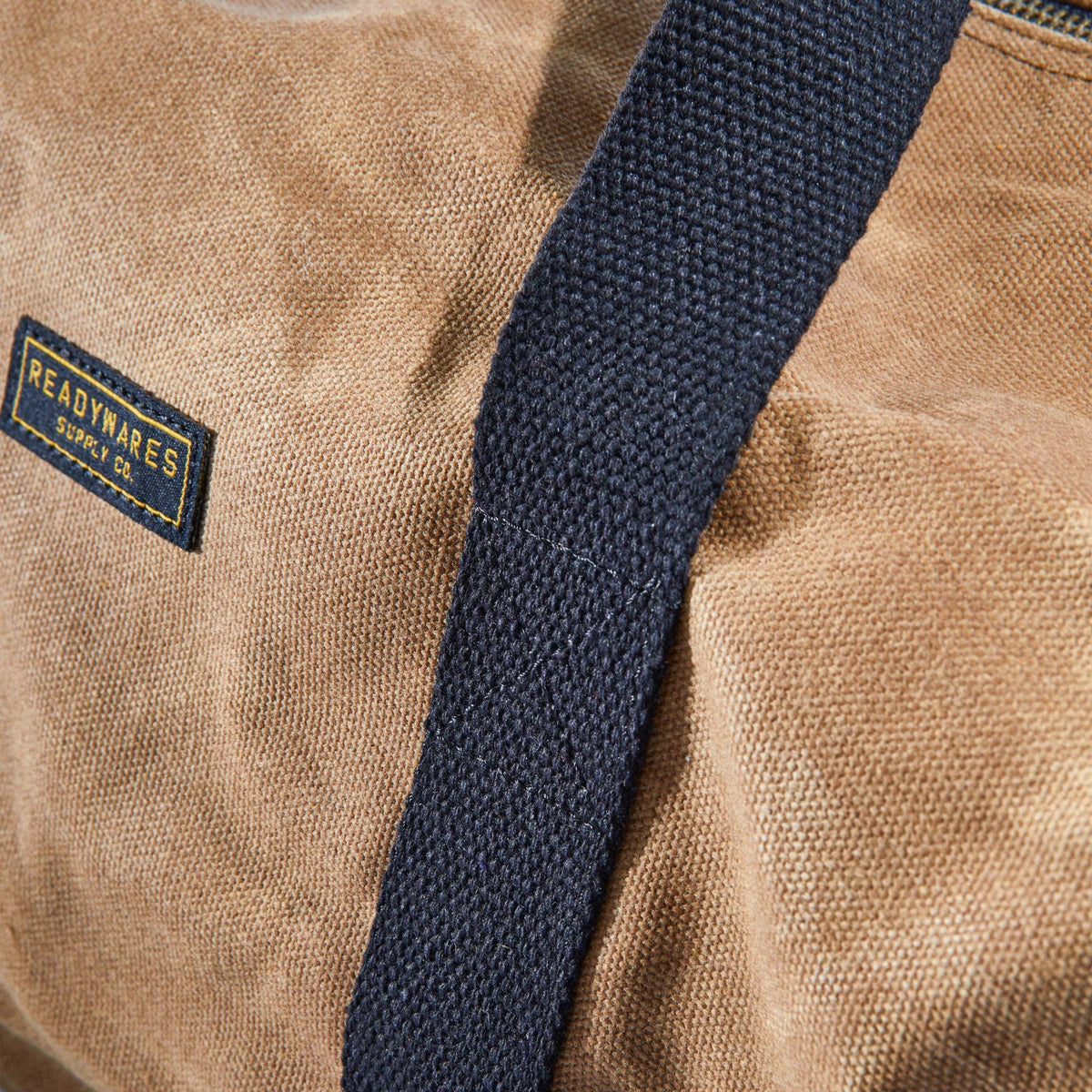 Close-up of the navy webbing strap and Readywares label on the duffel bag