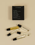 Five small perfume sample vials with black spray caps are arranged on a warm beige background below a black rectangular card labeled 'FOR EXPLORATION' and 'Pola Santo.' The vials contain clear and golden liquids, and several are labeled with scent names such as 'Sakura Odor,' 'Hawaii Scent,' 'Cactus Flower,' 'Desert Kosh,' and 'Pola Santo.