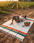 Person lying on a cream striped blanket with a picnic basket in a farm field