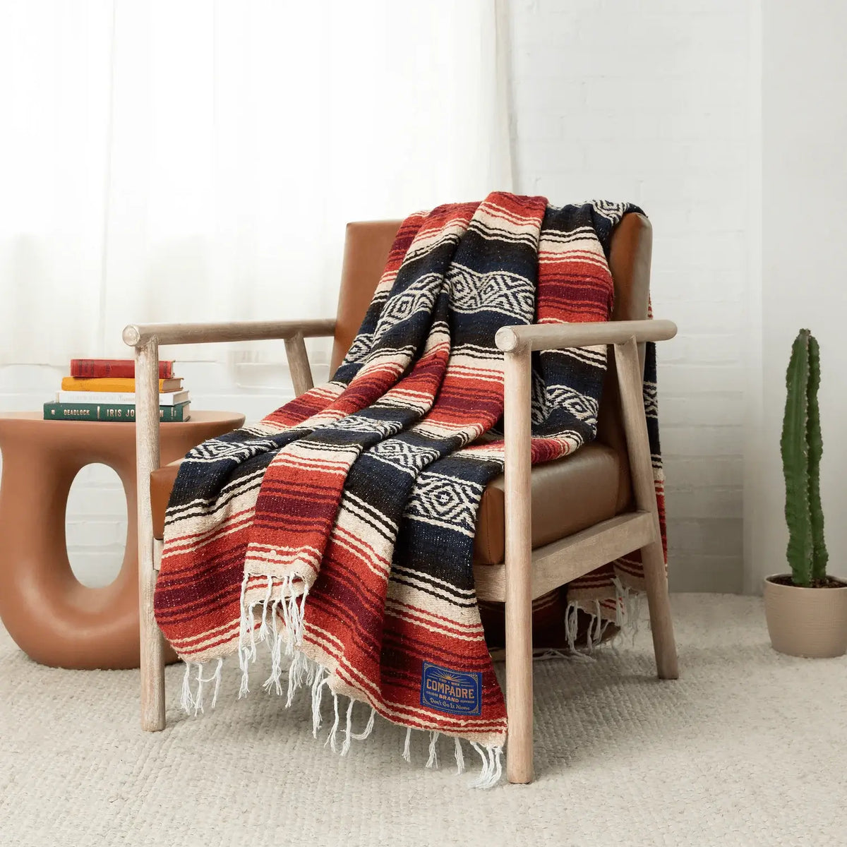 Navy, black, cream and red striped falsa blanket with a diamond band draped over a wooden armchair