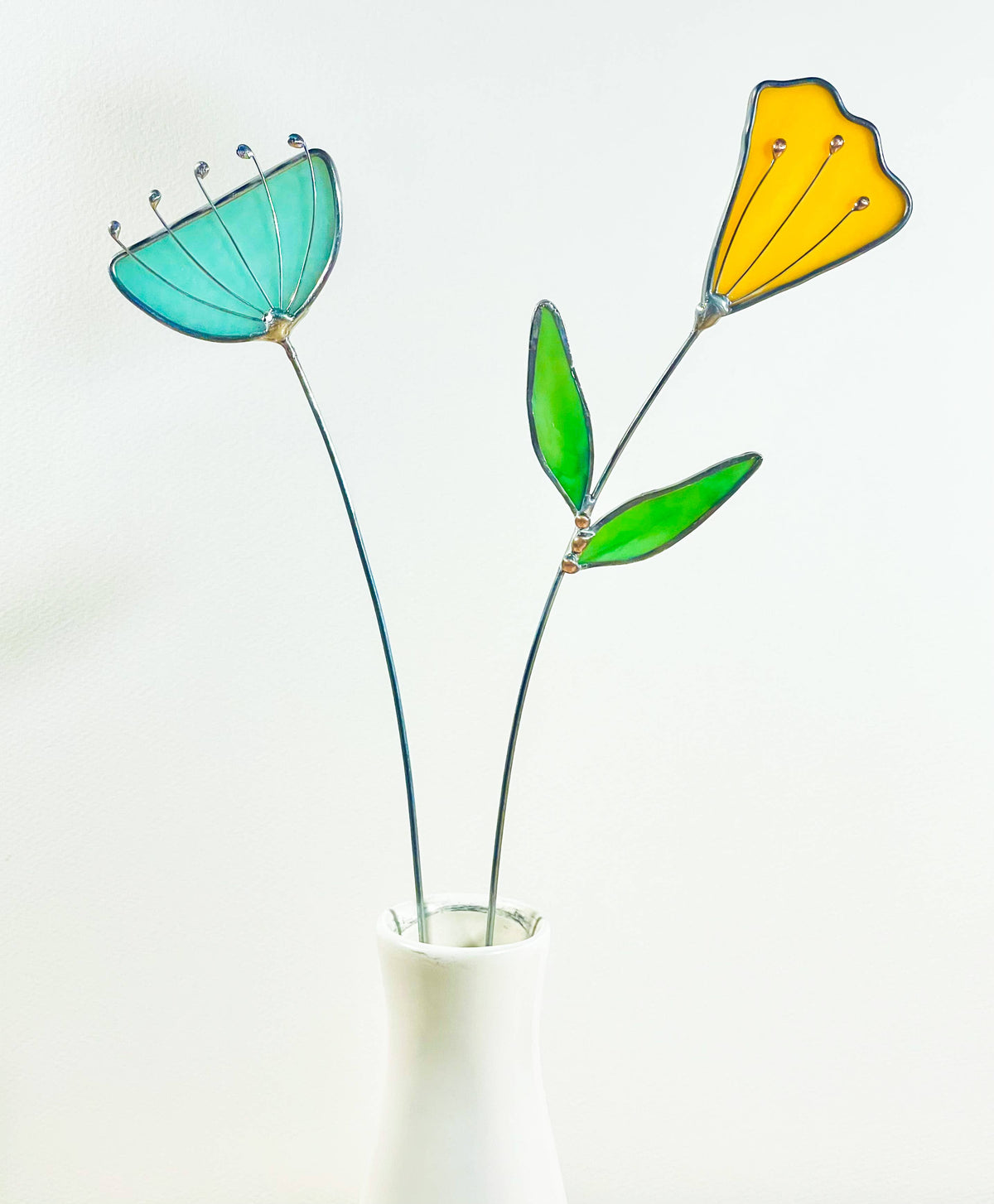 Stained glass aqua flower and yellow tulip stems in a white vase