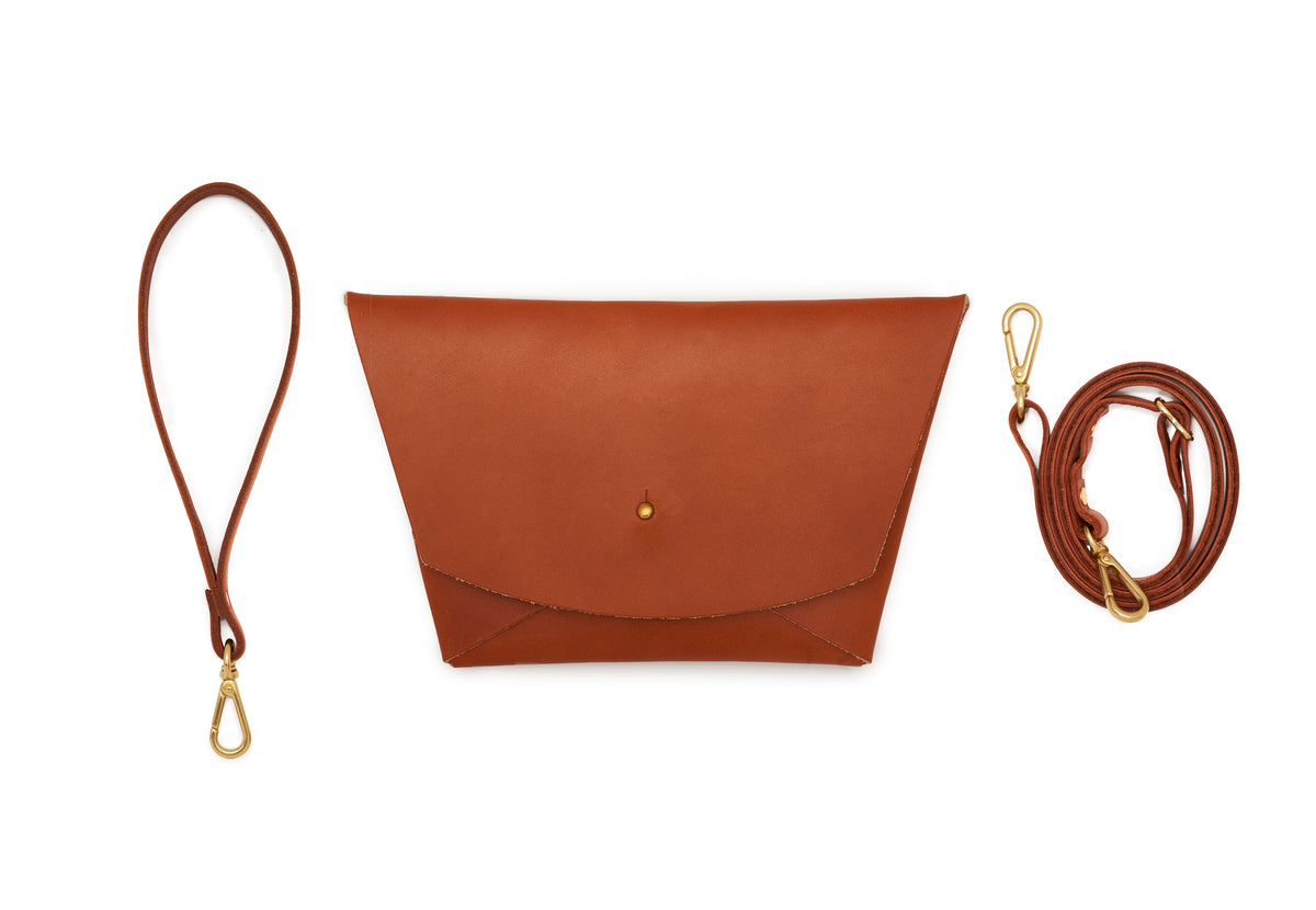 Tan leather clutch with wrist strap and adjustable crossbody strap on white