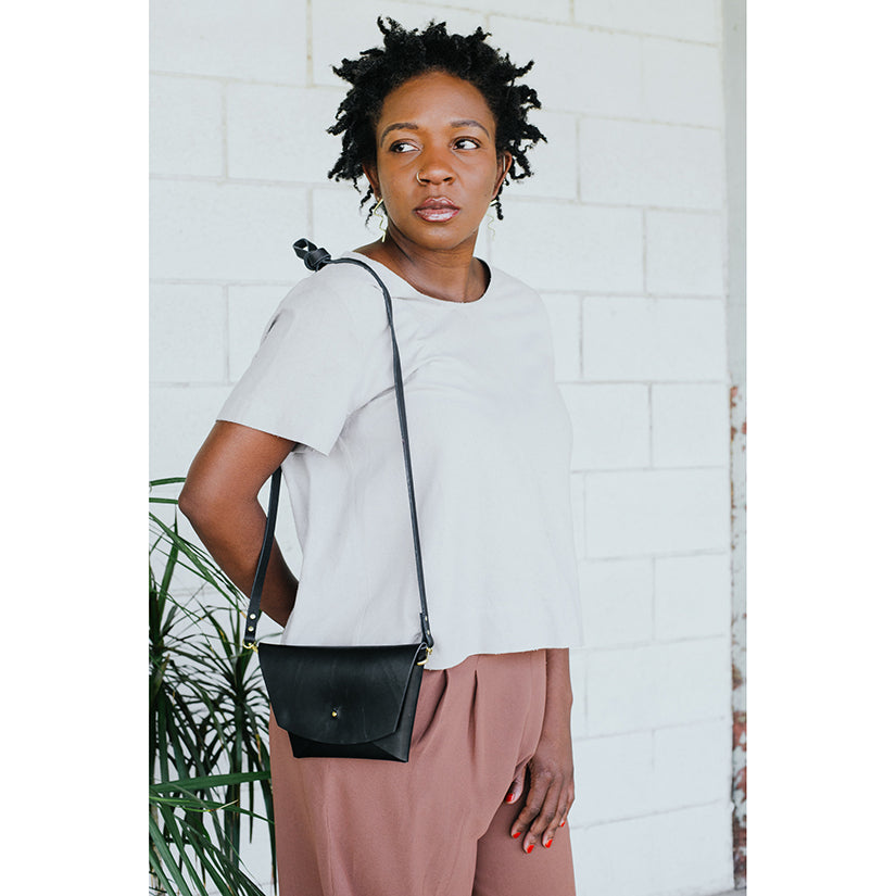 Model in a white tee wearing a black leather clutch as a crossbody bag