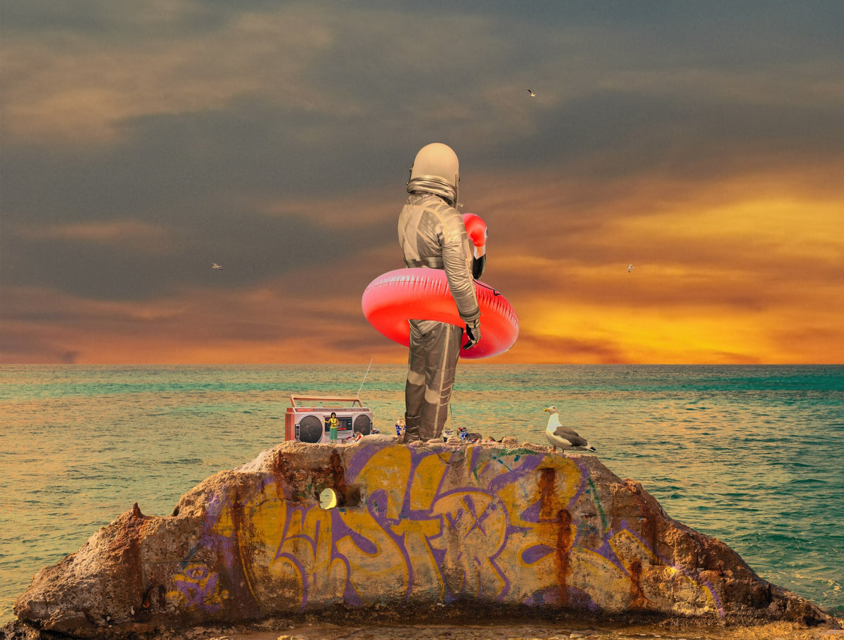 Art print of a figure in a red swim ring standing on a graffiti-covered rock by the sea at sunset