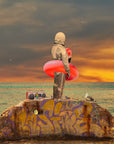 Art print of a figure in a red swim ring standing on a graffiti-covered rock by the sea at sunset